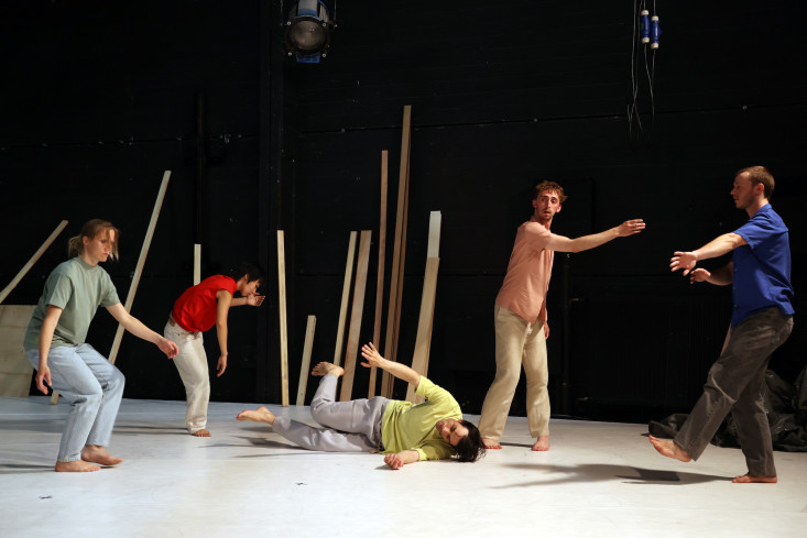 Fünf Menschen in bunter Alltagskleidung tanzen. Einer von ihnen liegt in der Mitte der Bühne auf dem Boden.