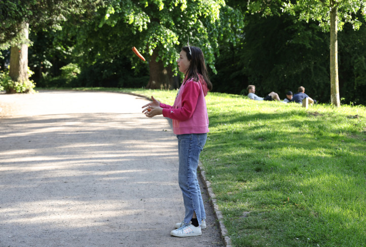 In einem Park steht eine junge Akteurin. Sie jongliert mit Möhren.