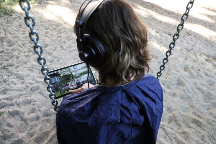 Eine Frau sitzt auf einer Schaukel. Sie hat Kopfhörer auf und schaut auf ein Tablet.