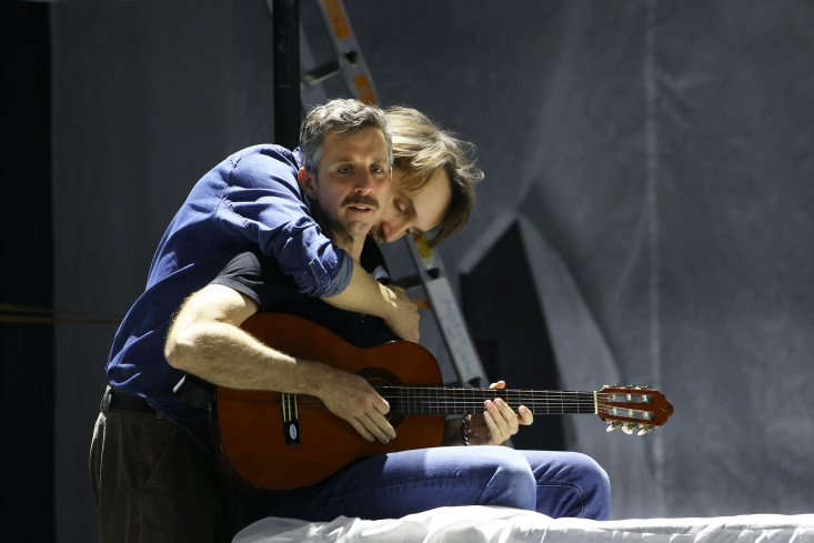 Ein Sänger spielt Gitarre. Ein anderer umarmt ihn dabei und legt seinen Kopf auf seine Schulter. Ein Sänger spielt Gitarre. Ein anderer umarmt ihn dabei und legt seinen Kopf auf seine Schulter.