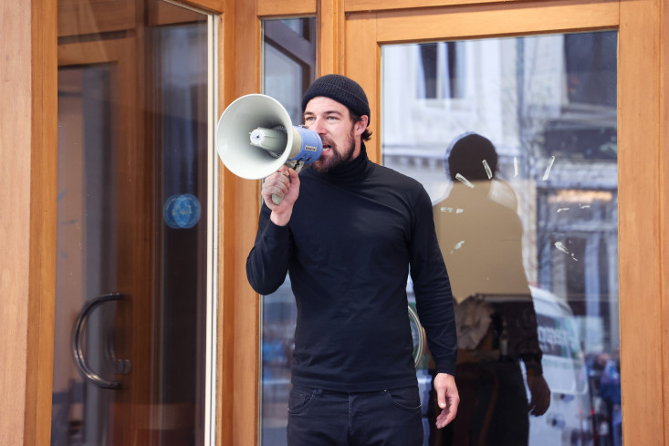 Ein schwarz gekleideter Mann ruft durch ein Megafon. Er steht im Eingang eines Ladens.