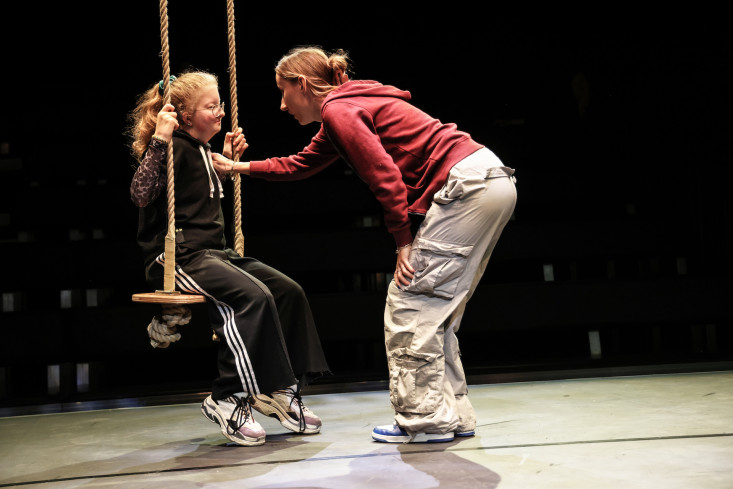 Eine Person sitzt auf einer Schaukel. Eine andere beugt sich zu ihr herunter. Eine Person sitzt auf einer Schaukel. Eine andere beugt sich zu ihr herunter.