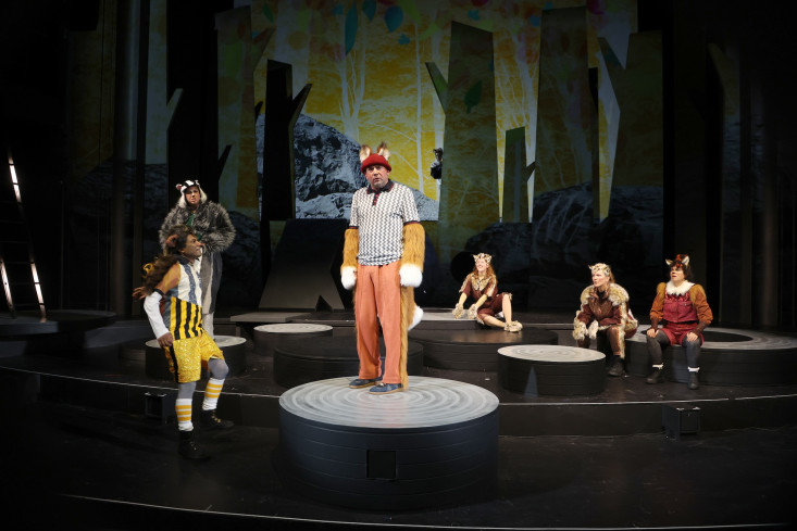 Sechs Personen sind auf der Bühne. Ein Schauspieler in einem Fuchskostüm steht vorn. Alle anderen sehen ihn an. Sechs Personen sind auf der Bühne. Ein Schauspieler in einem Fuchskostüm steht vorn. Alle anderen sehen ihn an.