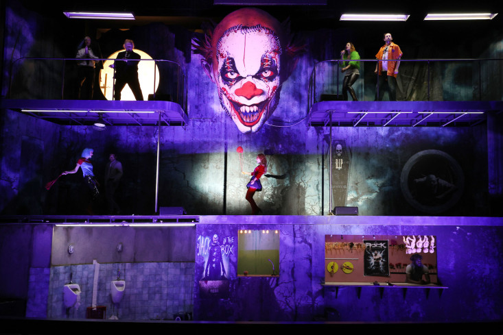 Das Bühnenbild besteht aus einer dreistöckigen Geisterbahn. In der Mitte hängt das Gesicht eines Horrorclowns. Auf den unterschiedlichen Stockwerken ist das Ensemble verteilt.