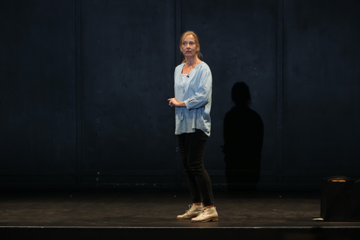 In schwarzer Hose, blauem Oberteil und weißen Schuhen steht die Schauspielerin seitlich auf der Bühne und spricht ins Publikum. In schwarzer Hose, blauem Oberteil und weißen Schuhen steht die Schauspielerin seitlich auf der Bühne und spricht ins Publikum.
