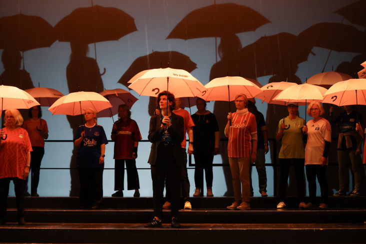 Viele Menschen mit aufgespannten Regenschirmen stehen auf der Bühne. Viele Menschen mit aufgespannten Regenschirmen stehen auf der Bühne.