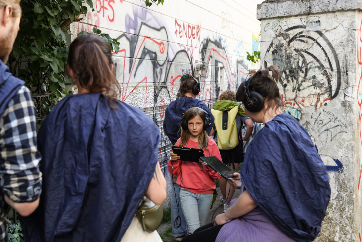 Eine Gruppe von Menschen mit Kopfhörern auf den Ohren und Tablets in den Händen. Sie stehen vor einer Wand irgendwo in der Stadt. Die Wand ist voller Graffiti.  Eine Gruppe von Menschen mit Kopfhörern auf den Ohren und Tablets in den Händen. Sie stehen vor einer Wand irgendwo in der Stadt. Die Wand ist voller Graffiti.
