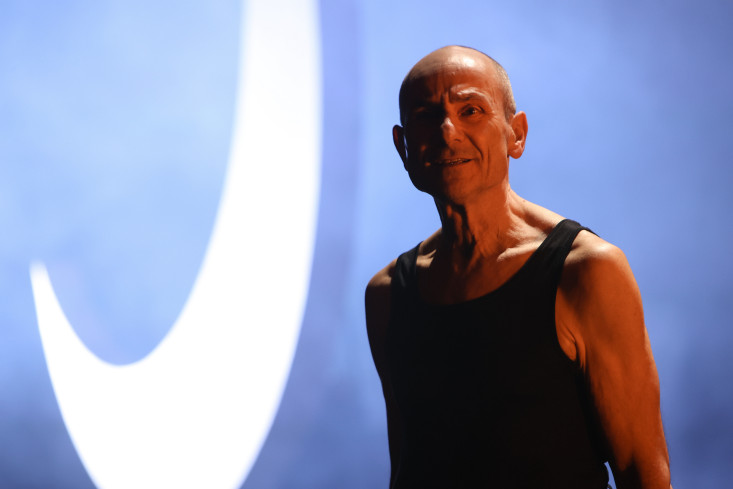 Ein Schauspieler steht vor einem blau beleuchteten Hintergrund. Hinter ihm ist eine hellbeleuchtete Mondsichel. Ein Schauspieler steht vor einem blau beleuchteten Hintergrund. Hinter ihm ist eine hellbeleuchtete Mondsichel.
