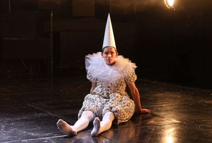 Ein Schauspieler in einem Clownskostüm sitzt auf dem Boden. Er trägt eine große Halskrause und einen spitzen Hut. Ein Schauspieler in einem Clownskostüm sitzt auf dem Boden. Er trägt eine große Halskrause und einen spitzen Hut.