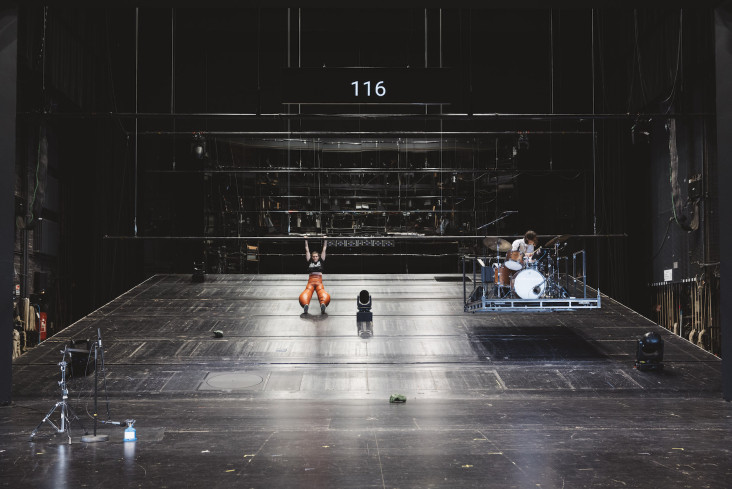 © Eike Walkenhorst | Auf dem Bild ist die ganze Bühne. Im hinteren Bühnenteil geht der Boden schräg nach oben. Vom Bühnenhimmel herunter hängt eine Stange. An der hält sich eine Schauspielerin fest. Neben ihr schwebt auf einem Podest ein Schlagzeug und der Schlagzeuger. Auf dem Bild ist die ganze Bühne. Im hinteren Bühnenteil geht der Boden schräg nach oben. Vom Bühnenhimmel herunter hängt eine Stange. An der hält sich eine Schauspielerin fest. Neben ihr schwebt auf einem Podest ein Schlagzeug und der Schlagzeuger.