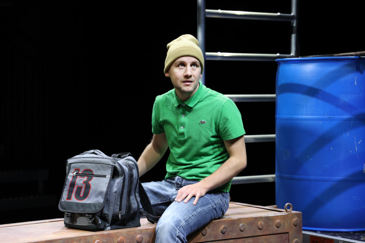 Ein Schauspieler sitzt mit Mütze und Schultasche auf einer Kiste. Ein Schauspieler sitzt mit Mütze und Schultasche auf einer Kiste.