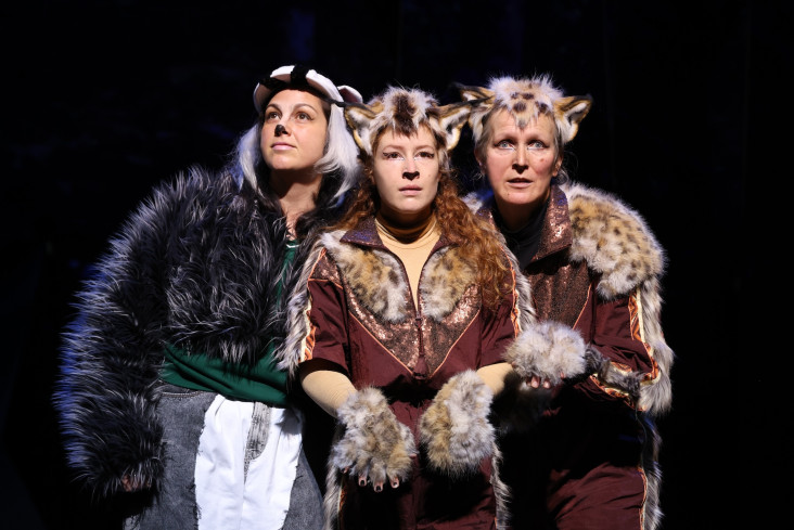 Drei Schauspielerinnen stehen eng beieinander und schauen nach vorn. Alle tragen Tierkostüme, eine sieht aus wie ein Dachs, zwei andere wie Raubkatzen. Drei Schauspielerinnen stehen eng beieinander und schauen nach vorn. Alle tragen Tierkostüme, eine sieht aus wie ein Dachs, zwei andere wie Raubkatzen.