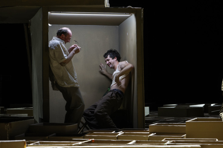 Zwei Schauspieler stehen sich in einem sehr kleinen Raum gegenüber. Beide lachen. Der eine lehnt an der Wand, der andere geht leicht in die Knie und stützt sich ab. Zwei Schauspieler stehen sich in einem sehr kleinen Raum gegenüber. Beide lachen. Der eine lehnt an der Wand, der andere geht leicht in die Knie und stützt sich ab.