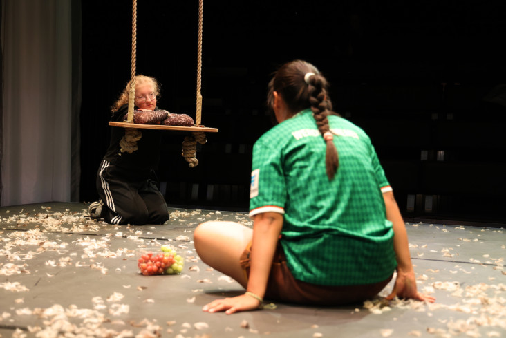 Eine Schauspielerin kniet vor der Schaukel. Ihr gegenüber sitzt eine andere Schauspielerin. Eine Schauspielerin kniet vor der Schaukel. Ihr gegenüber sitzt eine andere Schauspielerin.