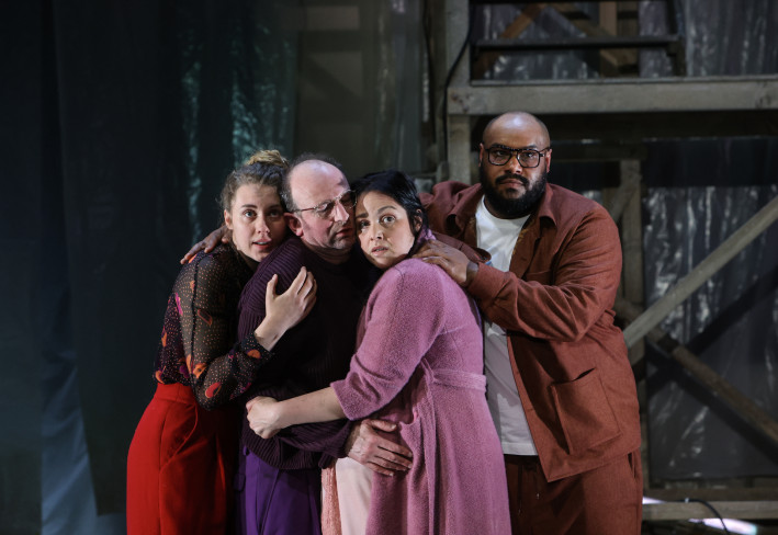 Vier Personen stehen eng beieinander. Sie halten sich gegenseitig fest. Drei von ihnen schauen in den Zuschauerraum.  Vier Personen stehen eng beieinander. Sie halten sich gegenseitig fest. Drei von ihnen schauen in den Zuschauerraum.