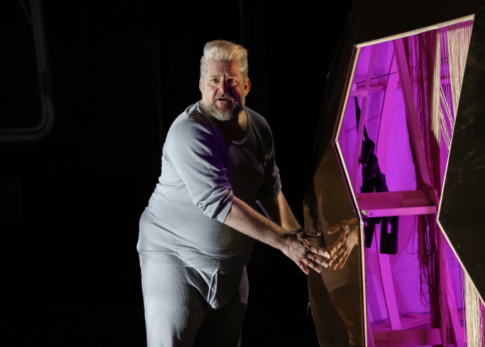 Ein Schauspieler steht in langer Unterwäsche neben einem goldenen Objekt. In dem Objekt ist eine Leiter sichtbar. Ein Schauspieler steht in langer Unterwäsche neben einem goldenen Objekt. In dem Objekt ist eine Leiter sichtbar.