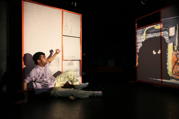 Ein Schauspieler sitzt nach hinten abgestützt auf dem Boden. Er blickt auf eine Zeichnung von einem großen schwarzen Monster. Ein Schauspieler sitzt nach hinten abgestützt auf dem Boden. Er blickt auf eine Zeichnung von einem großen schwarzen Monster.