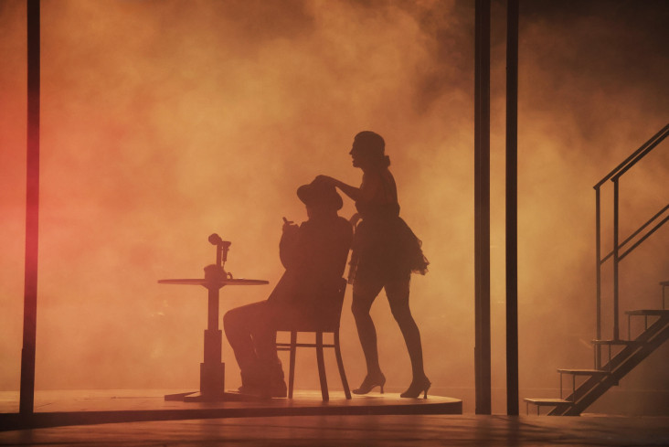 Zwei Silhouetten im Nebel und Gegenlicht. Ein Mann mit Hut sitzt an einem Tisch. Hinter ihm steht eine Frau in einem kurzen Kleid. Zwei Silhouetten im Nebel und Gegenlicht. Ein Mann mit Hut sitzt an einem Tisch. Hinter ihm steht eine Frau in einem kurzen Kleid.