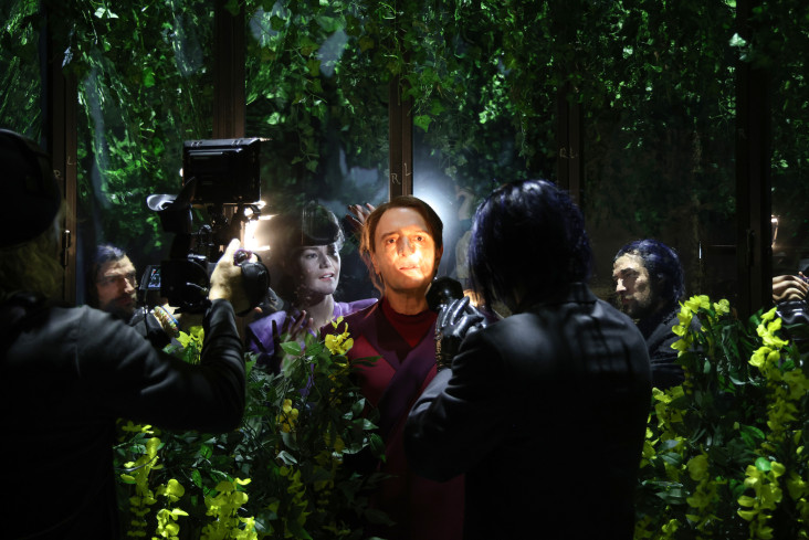 In der Mitte steht ein Schauspieler. Sein Gesicht wird von einer Taschenlampe angestrahlt. Er wird gefilmt. Hinter ihm steht eine Schauspielerin. Alle sind von großen Pflanzen umgeben. In der Mitte steht ein Schauspieler. Sein Gesicht wird von einer Taschenlampe angestrahlt. Er wird gefilmt. Hinter ihm steht eine Schauspielerin. Alle sind von großen Pflanzen umgeben.