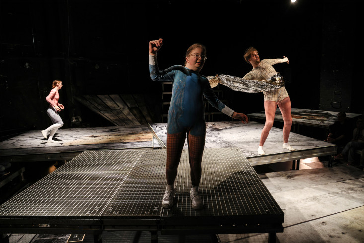 Auf der Bühne stehen drei Podeste. Auf jedem Podest steht eine Person. Auf der Bühne stehen drei Podeste. Auf jedem Podest steht eine Person.