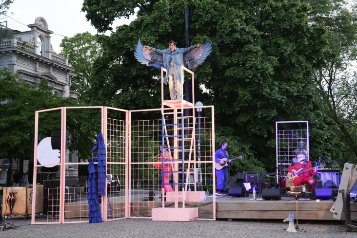 Auf einer Bühne auf dem Goetheplatz steht oben auf einer Leiter ein Schauspieler. Er trägt ein Kostüm mit großen, blauen Flügeln. Unten stehen andere, eine Band macht Musik. Auf einer Bühne auf dem Goetheplatz steht oben auf einer Leiter ein Schauspieler. Er trägt ein Kostüm mit großen, blauen Flügeln. Unten stehen andere, eine Band macht Musik.