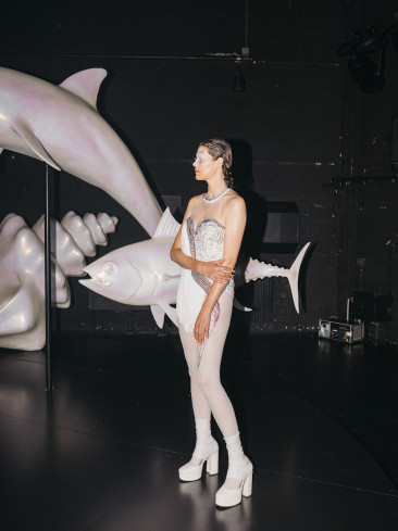 © Philip Frowein | Eine Schauspielerin trägt ein weißes Kleid und weiße Schuhe. Neben ihr sind Skulpturen von Fischen und Muscheln. Auch die Skulpturen sind weiß. Eine Schauspielerin trägt ein weißes Kleid und weiße Schuhe. Neben ihr sind Skulpturen von Fischen und Muscheln. Auch die Skulpturen sind weiß.