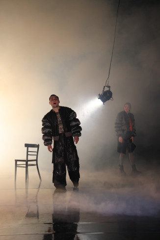 Ein Schauspieler steht neben einem Stuhl. Hinter ihm schwingt ein Scheinwerfer. Die Bühne ist in Nebel getaucht. Ein Schauspieler steht neben einem Stuhl. Hinter ihm schwingt ein Scheinwerfer. Die Bühne ist in Nebel getaucht.