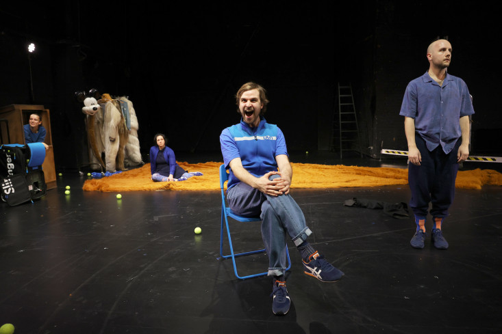 Ein Schauspieler sitzt auf einem Klappstuhl in der Bühnenmitte. Sein Mund ist aufgerissen. Die drei anderen sind hinter ihm verteilt. Ein Schauspieler sitzt auf einem Klappstuhl in der Bühnenmitte. Sein Mund ist aufgerissen. Die drei anderen sind hinter ihm verteilt.