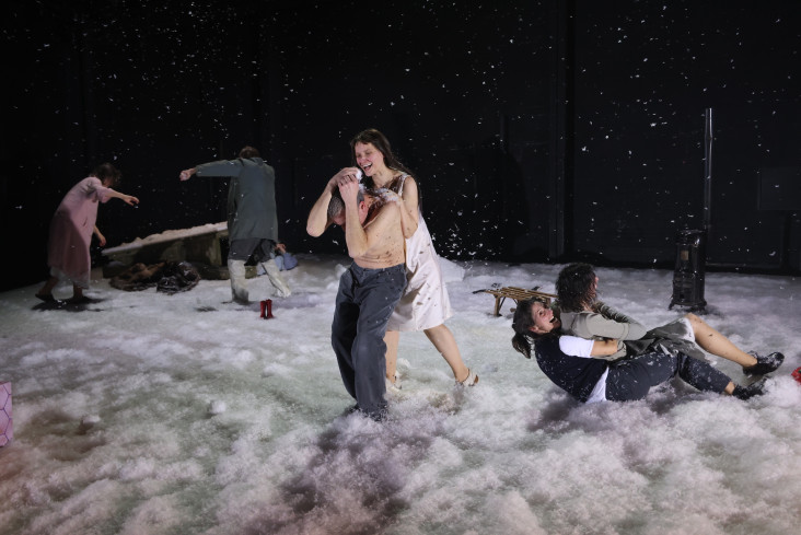 Die ganze Bühne ist mit Kunstschnee bedeckt. Vorn hält ein Mann mit nacktem Oberkörper die Arme über den Kopf. Eine Frau lehnt sich an ihn. Vier andere Personen sind noch auf der Bühne. Die ganze Bühne ist mit Kunstschnee bedeckt. Vorn hält ein Mann mit nacktem Oberkörper die Arme über den Kopf. Eine Frau lehnt sich an ihn. Vier andere Personen sind noch auf der Bühne.