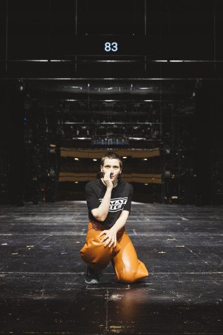 © Eike Walkenhorst | Vorn auf der Bühne kniet eine Schauspielerin. Sie trägt ein schwarzes T-Shirt und eine orangene Hose. Hinter ihr ist ein riesiger Spiegel. In dem spiegelt sich der Zuschauerraum. Vorn auf der Bühne kniet eine Schauspielerin. Sie trägt ein schwarzes T-Shirt und eine orangene Hose. Hinter ihr ist ein riesiger Spiegel. In dem spiegelt sich der Zuschauerraum.