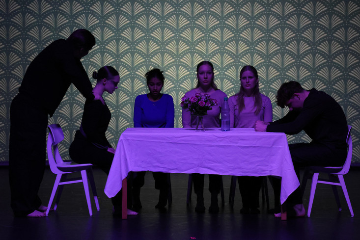 Fünf Jugendliche sitzen an einem Tisch. Eine Person steht hinter einer der Jugendlichen und legt seine Hände auf ihre Schultern. Auf dem Tisch steht ein Blumenstrauß. Fünf Jugendliche sitzen an einem Tisch. Eine Person steht hinter einer der Jugendlichen und legt seine Hände auf ihre Schultern. Auf dem Tisch steht ein Blumenstrauß.