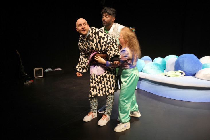 Ein Schauspieler trägt einen schwarz-weißen Mantel. Zwei andere Personen halten und stützten ihn. Ein Schauspieler trägt einen schwarz-weißen Mantel. Zwei andere Personen halten und stützten ihn.