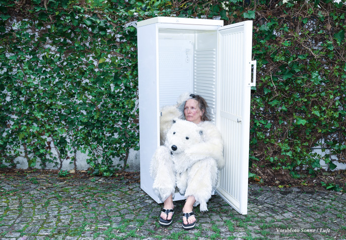 Eine Frau in einem Eisbärenkostüm sitzt in einem Kühlschrank. Den Kopf des Eisbären hält sie in ihren Händen.