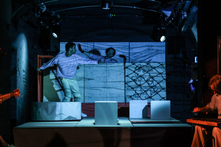 Die Bühne ist in blaues Licht getaucht. Zwei Personen bewegen sich zwischen den Kulissen. Die Bühne ist in blaues Licht getaucht. Zwei Personen bewegen sich zwischen den Kulissen.