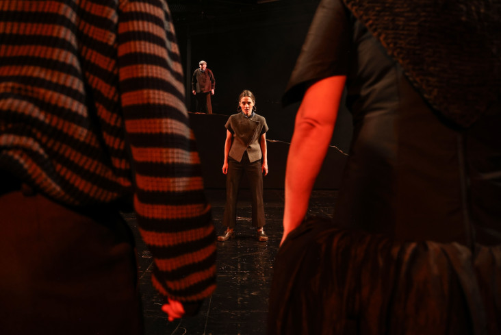 © Jörg Landsberg | Zwei Personen stehen mit dem Rücken zur Kamera. Ihnen gegenüber steht weiter hinten auf der Bühne eine Schauspielerin. Sie schaut die beiden an. Zwei Personen stehen mit dem Rücken zur Kamera. Ihnen gegenüber steht weiter hinten auf der Bühne eine Schauspielerin. Sie schaut die beiden an.