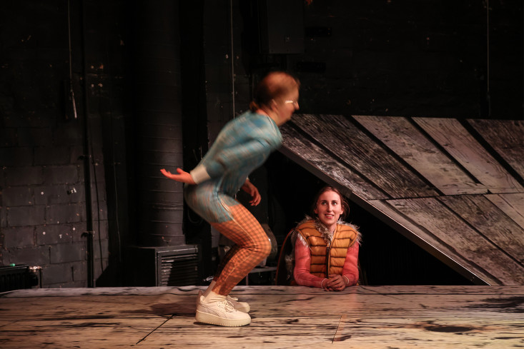 Eine Schauspielerin ist in voller Bewegung. Eine andere sitzt am Rand und schaut ihr zu.  Eine Schauspielerin ist in voller Bewegung. Eine andere sitzt am Rand und schaut ihr zu.