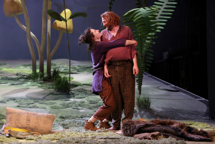 Eine Schauspielerin umarmt lachend einen Schauspieler. Im Hintergrund sind riesige Pilze und Farne. Eine Schauspielerin umarmt lachend einen Schauspieler. Im Hintergrund sind riesige Pilze und Farne.