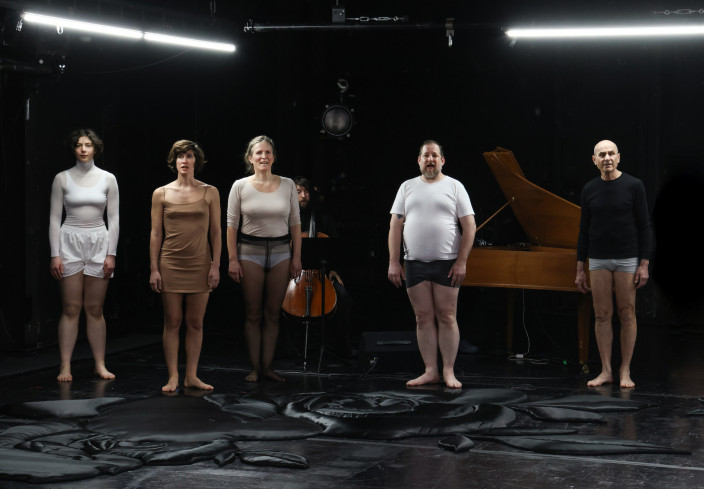 Fünf Personen stehen nebeneinander auf der Bühne. Hinter ihnen sitzt ein Musiker am Flügel, ein anderer am Cello. Fünf Personen stehen nebeneinander auf der Bühne. Hinter ihnen sitzt ein Musiker am Flügel, ein anderer am Cello.