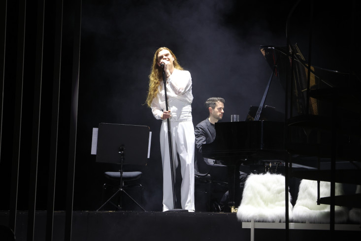Ein Sänger steht auf der Bühne und trägt einen weißen Anzug. Im Hintergrund sitzt ein Pianist. Ein Sänger steht auf der Bühne und trägt einen weißen Anzug. Im Hintergrund sitzt ein Pianist.