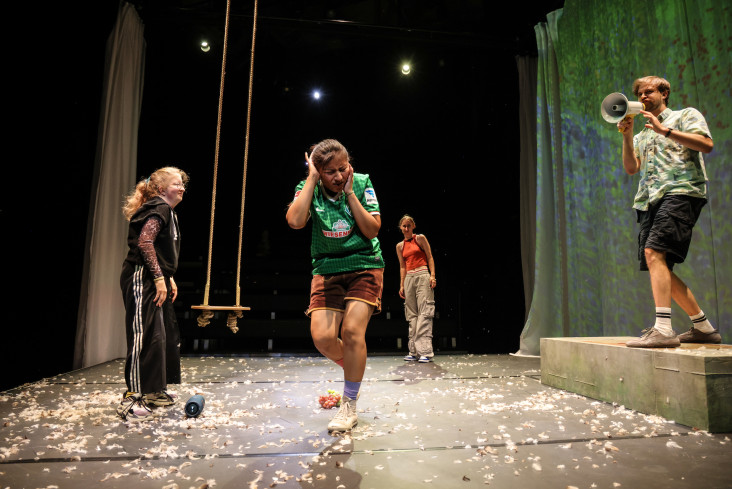 Ein Schauspieler ruft in ein Megafon. Eine Schauspielerin hält sich die Ohren zu. Zwei andere sehen ihn an.  Ein Schauspieler ruft in ein Megafon. Eine Schauspielerin hält sich die Ohren zu. Zwei andere sehen ihn an.