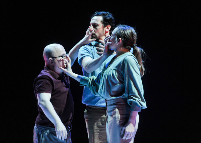 Drei Personen stehen dicht beieinander. Jede legt einer anderen Person die Hand auf den Mund. Drei Personen stehen dicht beieinander. Jede legt einer anderen Person die Hand auf den Mund.