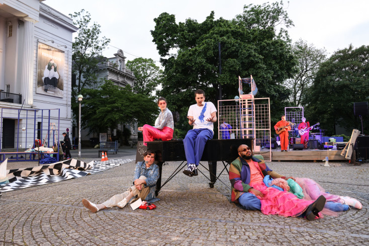 Auf dem Goetheplatz steht ein Flügel. Auf dem sitzen zwei Personen, drei andere sitzen auf dem Boden davor. Hinten spielt die Band. Auf dem Goetheplatz steht ein Flügel. Auf dem sitzen zwei Personen, drei andere sitzen auf dem Boden davor. Hinten spielt die Band.