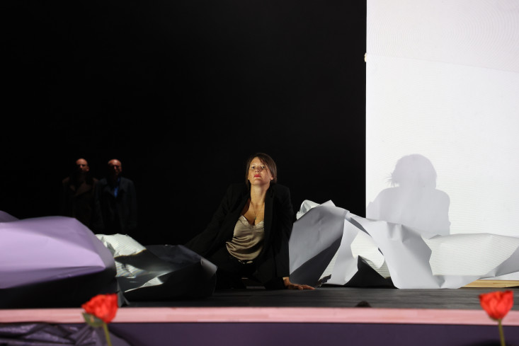 Eine Schauspielerin sitzt auf dem Boden. Neben ihr liegen abgerissene Papierbahnen. Eine Schauspielerin sitzt auf dem Boden. Neben ihr liegen abgerissene Papierbahnen.