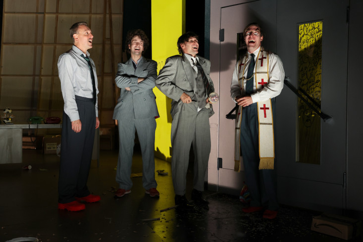 Vier Schauspieler stehen nebeneinander und lachen mit geöffneten Mündern. Drei tragen einen Anzug, einer ist gekleidet wie ein Priester. Vier Schauspieler stehen nebeneinander und lachen mit geöffneten Mündern. Drei tragen einen Anzug, einer ist gekleidet wie ein Priester.