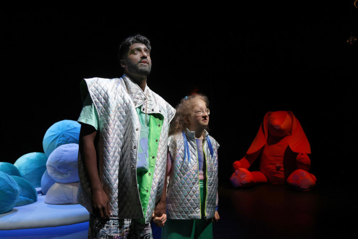 Ein Schauspieler und eine Schauspielerin stehen nebeneinander. Sie halten sich an den Händen. Im Hintergrund sitzt ein großer, roter Stoffhase. Ein Schauspieler und eine Schauspielerin stehen nebeneinander. Sie halten sich an den Händen. Im Hintergrund sitzt ein großer, roter Stoffhase.