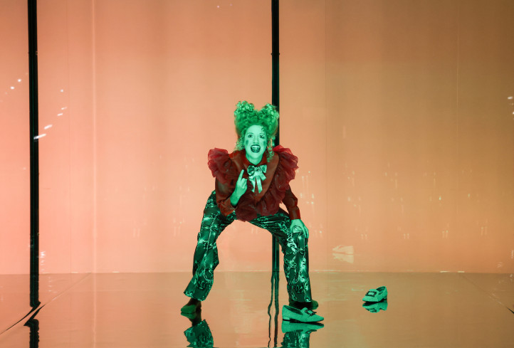 Eine Schauspielerin steht mit gebeugten Knien und nach vorn gelehnt auf der Bühne. Sie trägt eine Rokoko-Perücke und eine Bluse mit großen Rüschen. Eine Schauspielerin steht mit gebeugten Knien und nach vorn gelehnt auf der Bühne. Sie trägt eine Rokoko-Perücke und eine Bluse mit großen Rüschen.