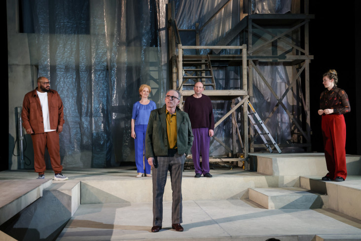 Fünf Personen stehen auf der Bühne. Alle halten Abstand zueinander. Im Hintergrund ist eine Haus-Baustelle zu erkennen. Plastikplanen hängen hinter einem Holzgerüst. Fünf Personen stehen auf der Bühne. Alle halten Abstand zueinander. Im Hintergrund ist eine Haus-Baustelle zu erkennen. Plastikplanen hängen hinter einem Holzgerüst.