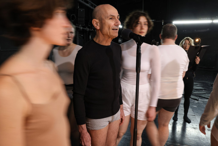 Das Ensemble steht dicht beieinander. Ein Schauspieler spricht ins Mikrofon. Das Ensemble steht dicht beieinander. Ein Schauspieler spricht ins Mikrofon.