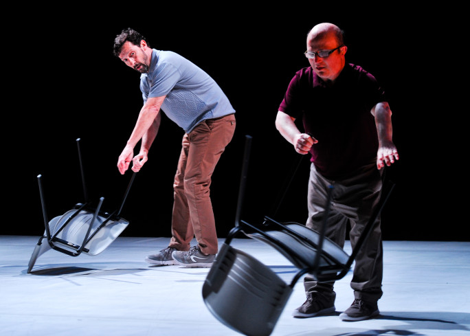 Zwei Personen sind auf der Bühne. Beide haben einen Stuhl an seinen Beinen gefasst. Zwei Personen sind auf der Bühne. Beide haben einen Stuhl an seinen Beinen gefasst.