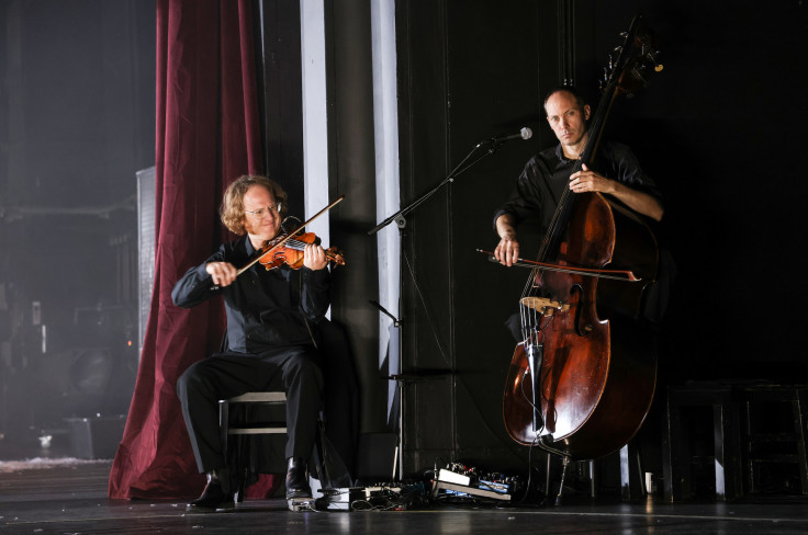 Zwei Musiker sind an der Seite der Bühne. Einer sitzt und spielt Geige, ein anderer Kontrabass. Zwei Musiker sind an der Seite der Bühne. Einer sitzt und spielt Geige, ein anderer Kontrabass.
